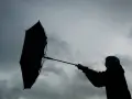 Silhouette einer Person mit einem aufgewehten Regenschirm vor dramatischem Himmel. Der **Orkan** kämpft gegen den Schirm.