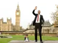 Der größte Mensch der Welt winkt vor dem Big Ben in London. Neben ihm steht ein Mann von sehr kleinem Wuchs.