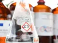 Ein Becherglas mit Salpetersäure (HNO3) und einem Gefahrensymbol. Im Hintergrund stehen weitere braune Glasflaschen mit Chemikalien.