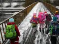 Kinder mit bunten Rucksäcken auf verschneiter Brücke, unterwegs zu den weihnachtsferien mv 2025.