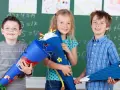 Drei Kinder mit Schultüten vor einer Tafel. Die Einschulung in Sachsen-Anhalt 2025 wird hier fröhlich gefeiert.