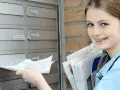 Ein junges Mädchen mit Zahnspange verteilt Zeitungen als Ferienjob. Sie steckt gerade eine Zeitung in einen Briefkasten.