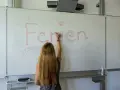 Frau schreibt "Ferien" an Tafel, Vorfreude auf Pfingstferien Rheinland-Pfalz.