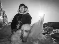 Ein Mann in traditioneller Inuit-Kleidung sitzt in eisiger Landschaft. Die Sonne scheint hell.