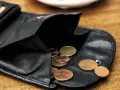 Schwarzes Lederportemonnaie mit Münzen. Die wenigen Münzen symbolisieren die Opportunitätskosten, wenn man sich für eine Ausgabe entscheidet.