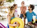 Lachende Familie am Strand mit gelbem Schwimmring und Getränken.