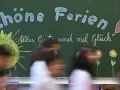 Kreidetafel mit "Schöne Ferien" und einem lachenden Smiley, bereit für die herbstferien 2025 nrw. Kinder huschen vorbei.