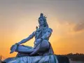 Eine riesige Statue von Shiva sitzt in meditativer Haltung vor einem warmen Sonnenuntergang.
