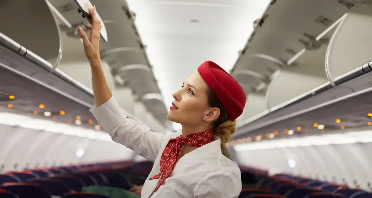 Flugbegleiterin schließt Gepäckfach. Ein Beruf, der mehr als nur das Flugbegleiter Gehalt bietet.