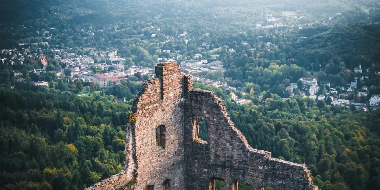 Ruinen einer Burg mit Blick auf eine Stadt und bewaldete Hügel.