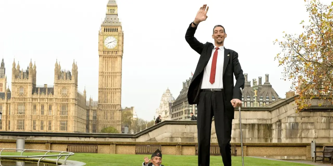 Der größte Mensch der Welt winkt vor dem Big Ben in London. Neben ihm steht ein Mann von sehr kleinem Wuchs.