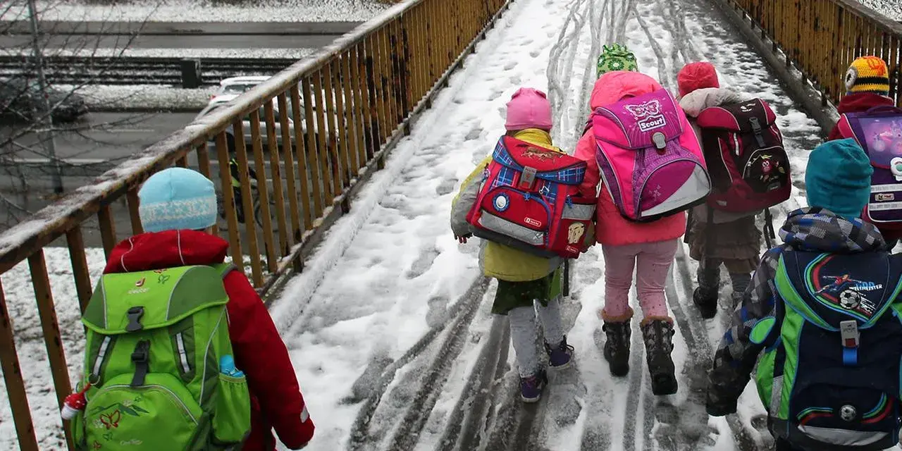 Kinder mit bunten Rucksäcken auf verschneiter Brücke, unterwegs zu den weihnachtsferien mv 2025.