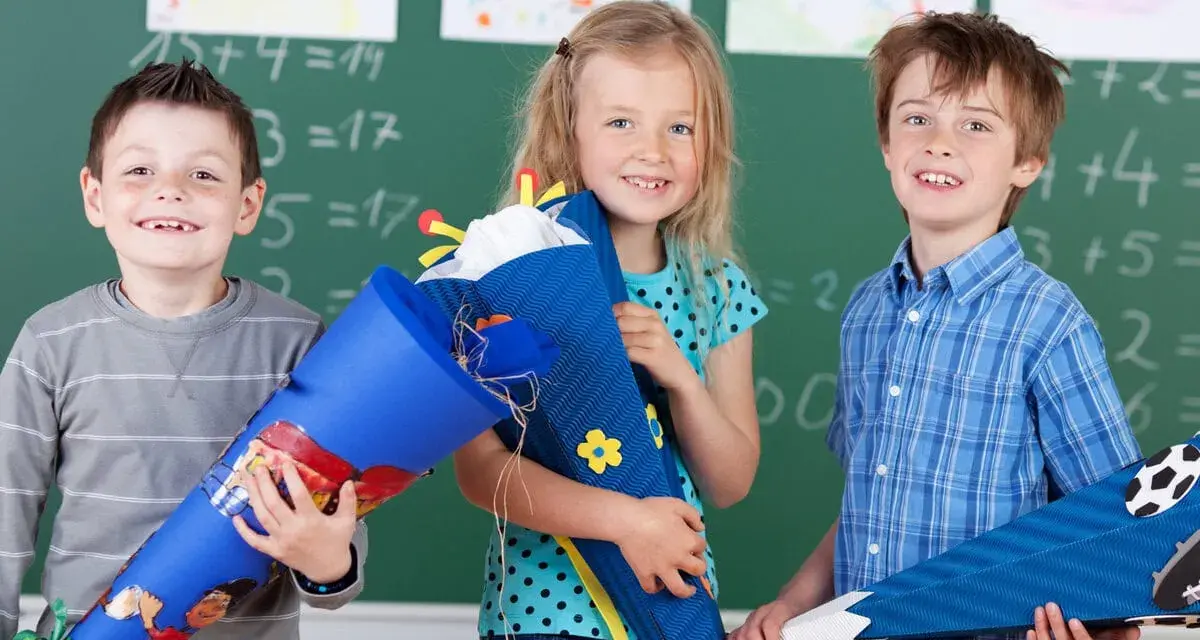 Drei Kinder mit Schultüten vor einer Tafel. Die Einschulung in Sachsen-Anhalt 2025 wird hier fröhlich gefeiert.