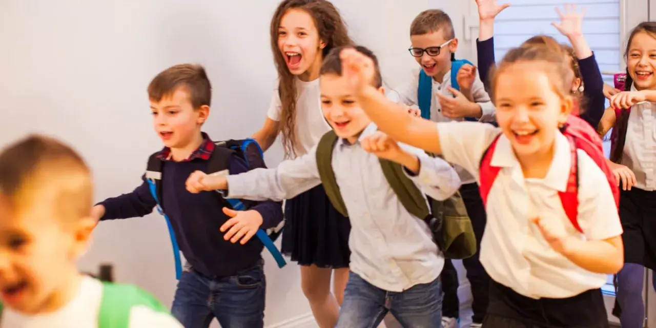 Fröhliche Schulkinder mit Rucksäcken rennen los.
