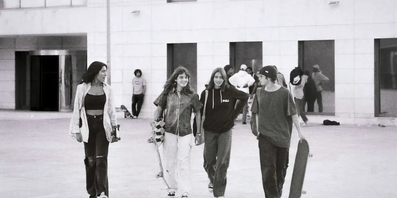 Vier junge Leute, die zur genz gehören, gehen mit Skateboards vor einem modernen Gebäude.