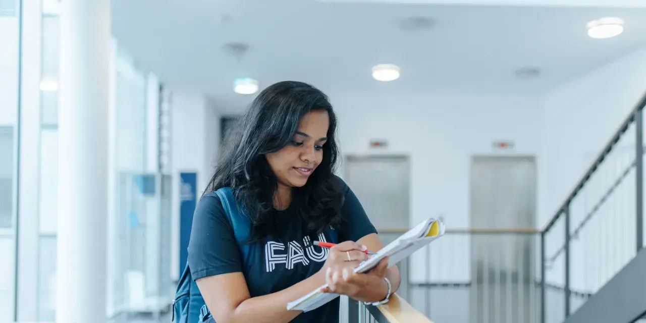 Junge Frau mit Rucksack lernt für die Hochschulreife in einem modernen Gebäude.