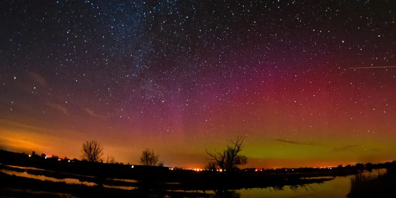Ein atemberaubendes polarlicht tanzt über einem sternenklaren Himmel, reflektiert in einem ruhigen Gewässer.