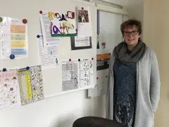 Lehrerin mit Lernmaterialien, darunter ein Kreuzworträtsel mit Gegenteilen und eine Liste von Verben, die das present participle zeigen.