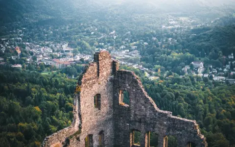 Ruinen einer Burg mit Blick auf eine Stadt und bewaldete Hügel.