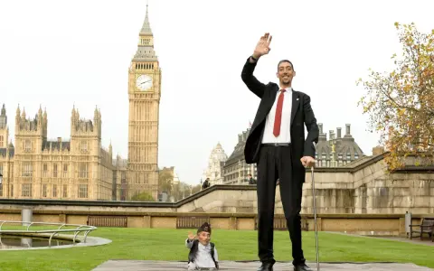 Der größte Mensch der Welt winkt vor dem Big Ben in London. Neben ihm steht ein Mann von sehr kleinem Wuchs.