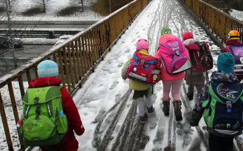 Kinder mit bunten Rucksäcken auf verschneiter Brücke, unterwegs zu den weihnachtsferien mv 2025.