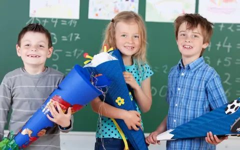 Drei Kinder mit Schultüten vor einer Tafel. Die Einschulung in Sachsen-Anhalt 2025 wird hier fröhlich gefeiert.
