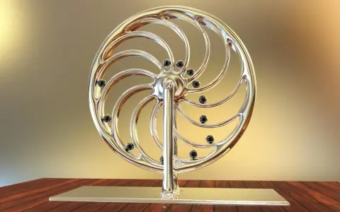 Glänzendes Rad mit schwarzen Kugeln, das an ein Perpetuum mobile erinnert, steht auf einem Holztisch.