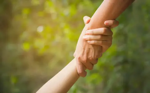 Zwei Hände greifen ineinander, ein Symbol für **Altruismus** und gegenseitige Hilfe im sanften Licht.