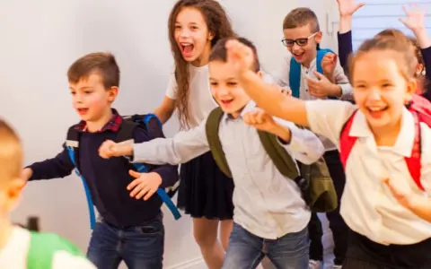 Fröhliche Schulkinder mit Rucksäcken rennen los.