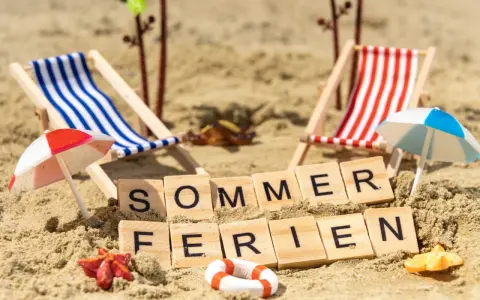 Strandkörbchen, Palmen und die Worte "Sommerferien" im Sand. Berlin wartet auf die Sommerferien 2026!