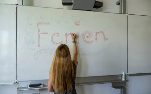 Frau schreibt "Ferien" an Tafel, Vorfreude auf Pfingstferien Rheinland-Pfalz.