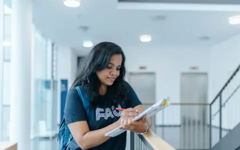 Junge Frau mit Rucksack lernt für die Hochschulreife in einem modernen Gebäude.