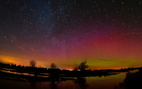 Ein atemberaubendes polarlicht tanzt über einem sternenklaren Himmel, reflektiert in einem ruhigen Gewässer.