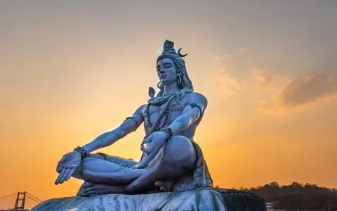 Eine riesige Statue von Shiva sitzt in meditativer Haltung vor einem warmen Sonnenuntergang.