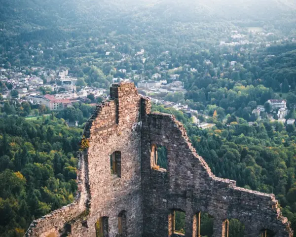 Ruinen einer Burg mit Blick auf eine Stadt und bewaldete Hügel.