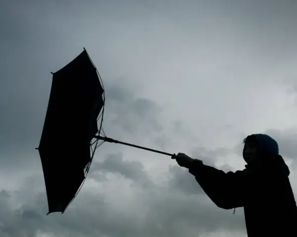 Silhouette einer Person mit einem aufgewehten Regenschirm vor dramatischem Himmel. Der **Orkan** kämpft gegen den Schirm.