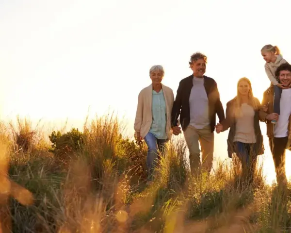 Eine Familie, die durch hohes Gras spaziert, zeigt eine schöne Generationen übersicht. Großeltern halten Händchen, Eltern gehen nebeneinander, ein Kind sitzt auf den Schultern des Vaters, ein weiterer Junge läuft daneben.