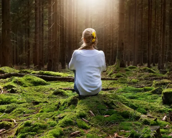 Frau sitzt im Wald auf moosbewachsenem Boden, umgeben von Bäumen. Sonnenstrahlen fallen durch das Blätterdach und erzeugen eine Atmosphäre der Katharsis.