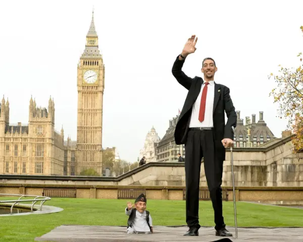 Der größte Mensch der Welt winkt vor dem Big Ben in London. Neben ihm steht ein Mann von sehr kleinem Wuchs.