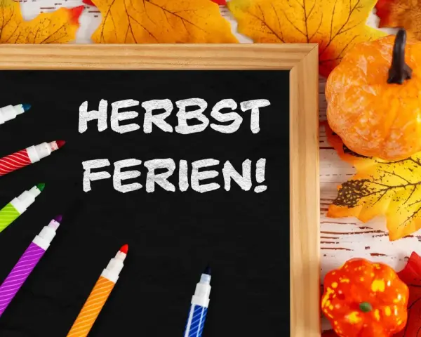 Bunte Stifte und Herbstdeko umrahmen eine Tafel mit der Aufschrift "Herbstferien!". Zeit für die Herbstferien Baden-Württemberg 2025!