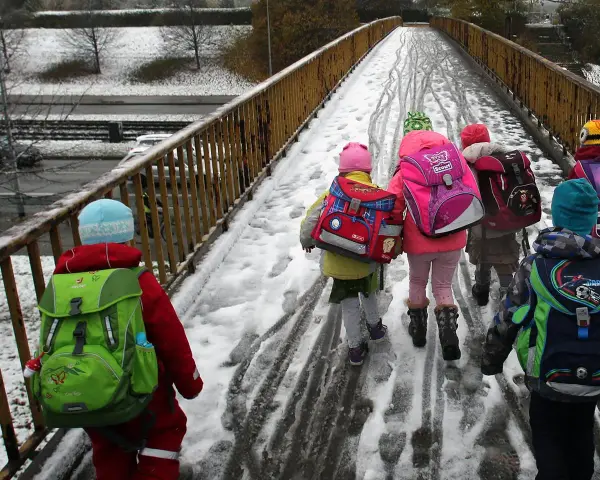 Kinder mit bunten Rucksäcken auf verschneiter Brücke, unterwegs zu den weihnachtsferien mv 2025.