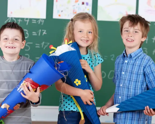 Drei Kinder mit Schultüten vor einer Tafel. Die Einschulung in Sachsen-Anhalt 2025 wird hier fröhlich gefeiert.