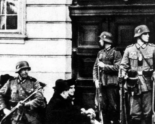 Soldaten der Gestapo stehen Wache. Ein Mann mit Gewehr im Vordergrund, zwei weitere im Hintergrund.