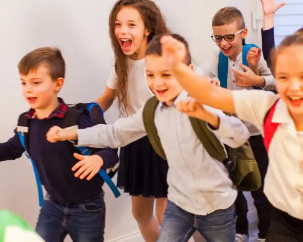 Fröhliche Schulkinder mit Rucksäcken rennen los.