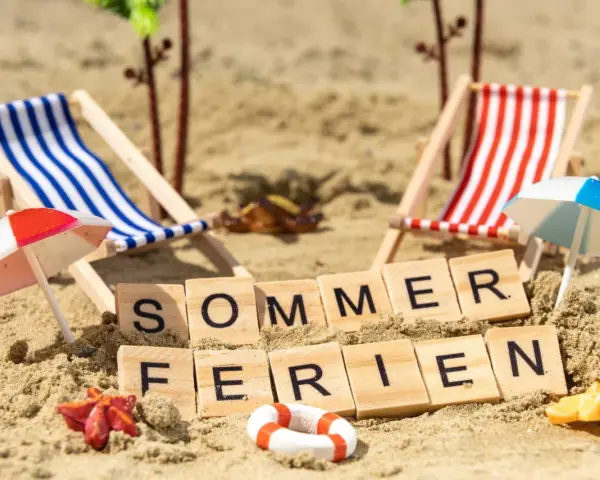 Strandkörbchen, Palmen und die Worte "Sommerferien" im Sand. Berlin wartet auf die Sommerferien 2026!