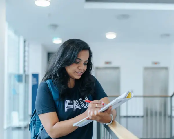 Junge Frau mit Rucksack lernt für die Hochschulreife in einem modernen Gebäude.