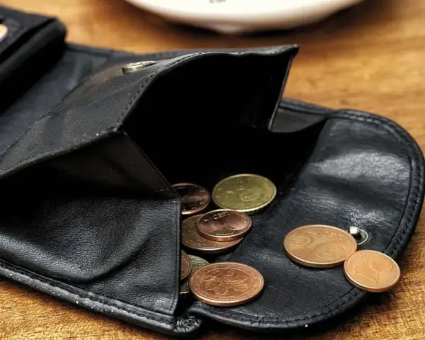 Schwarzes Lederportemonnaie mit Münzen. Die wenigen Münzen symbolisieren die Opportunitätskosten, wenn man sich für eine Ausgabe entscheidet.