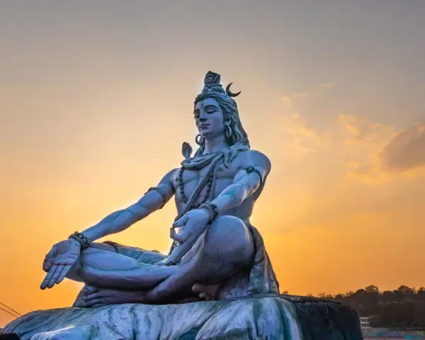 Eine riesige Statue von Shiva sitzt in meditativer Haltung vor einem warmen Sonnenuntergang.