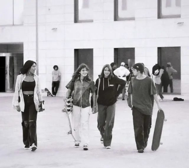 Vier junge Leute, die zur genz gehören, gehen mit Skateboards vor einem modernen Gebäude.