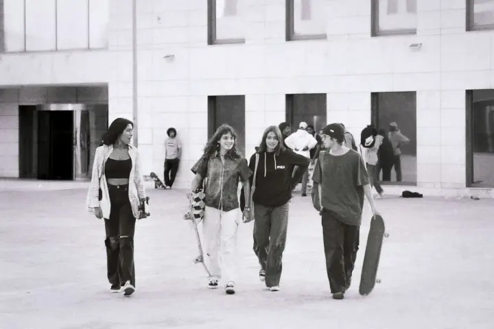Vier junge Leute, die zur genz gehören, gehen mit Skateboards vor einem modernen Gebäude.